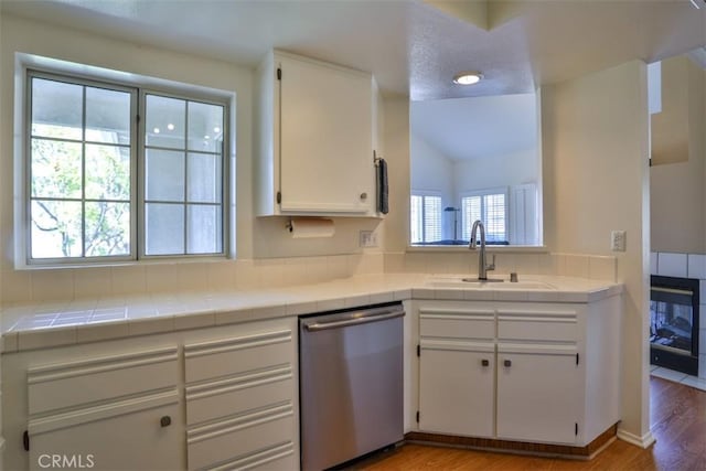 kitchen featuring white cabinets, a sink, tile counters, light wood-type flooring, and stainless steel dishwasher