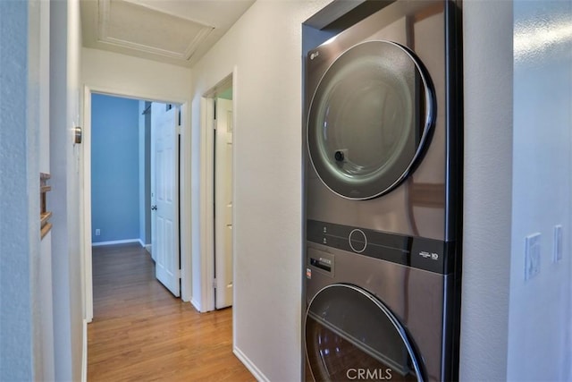 washroom featuring laundry area, attic access, stacked washer and dryer, baseboards, and light wood-style floors