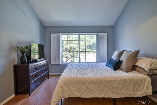 bedroom featuring baseboards, wood finished floors, and lofted ceiling