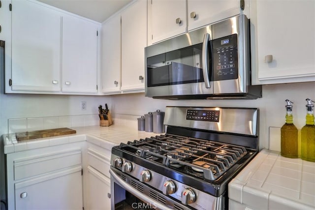 kitchen with tile counters, stainless steel appliances, and white cabinetry