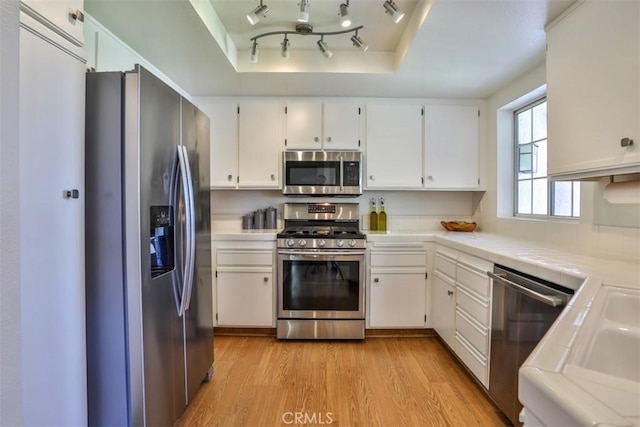 kitchen with white cabinets, tile countertops, appliances with stainless steel finishes, and light wood-type flooring