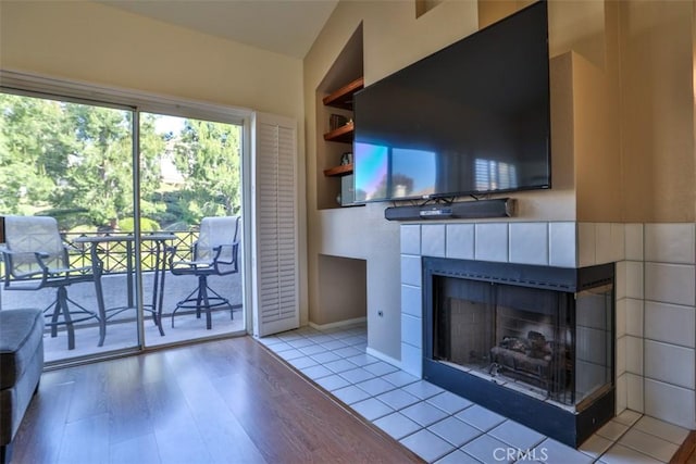 living room featuring baseboards, wood finished floors, lofted ceiling, and a tile fireplace