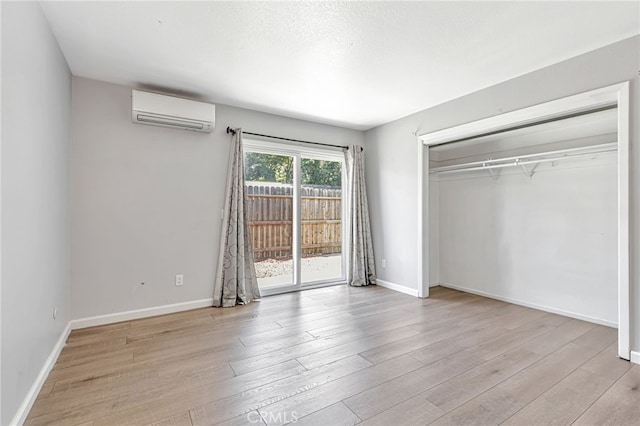 unfurnished bedroom with an AC wall unit, access to exterior, baseboards, wood finished floors, and a closet