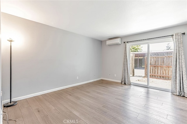 unfurnished room with baseboards, a wall mounted AC, and wood finished floors