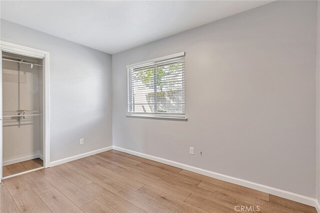 unfurnished bedroom with baseboards, a closet, and light wood-type flooring
