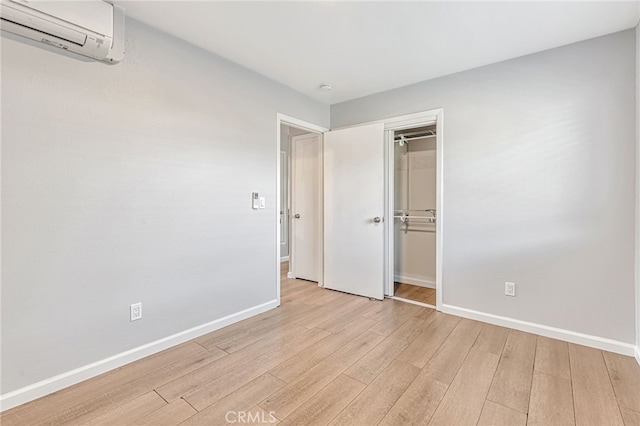 unfurnished bedroom with baseboards, light wood-style flooring, and a wall mounted AC