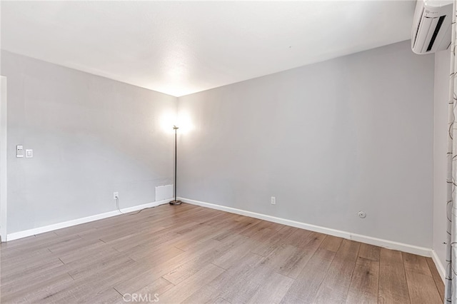 spare room featuring light wood-style floors, baseboards, and a wall mounted air conditioner