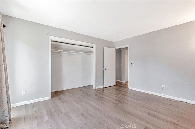 unfurnished bedroom with baseboards, light wood-style flooring, and a closet