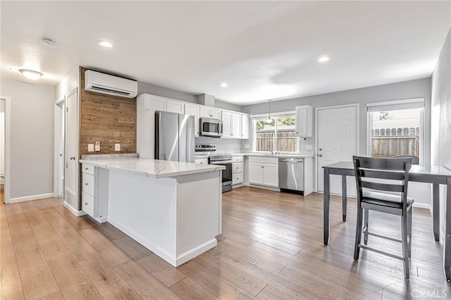 kitchen featuring white cabinets, appliances with stainless steel finishes, light wood finished floors, an AC wall unit, and a peninsula