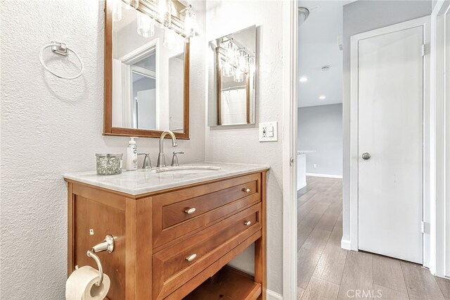 bathroom with vanity, a textured wall, baseboards, and wood finished floors