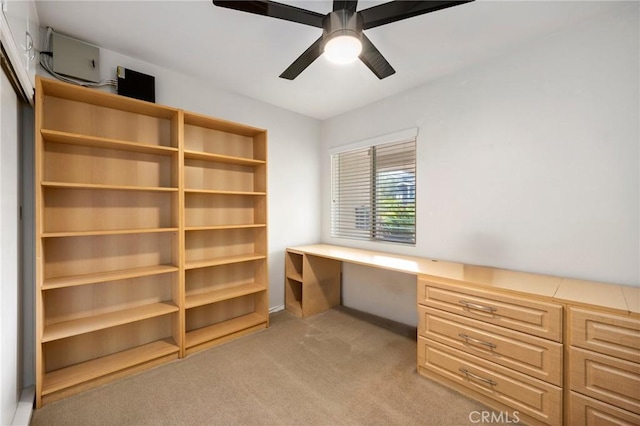 unfurnished office featuring built in study area, a ceiling fan, and light carpet