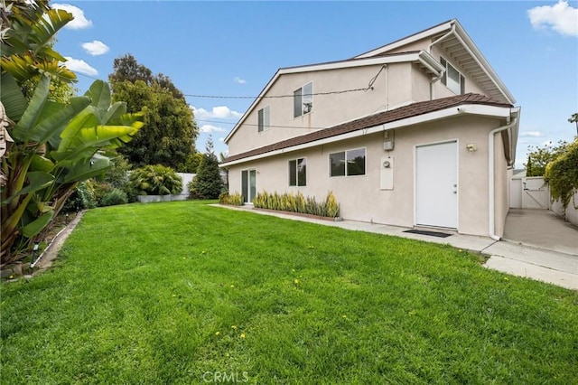 rear view of house with a gate, stucco siding, a yard, and fence