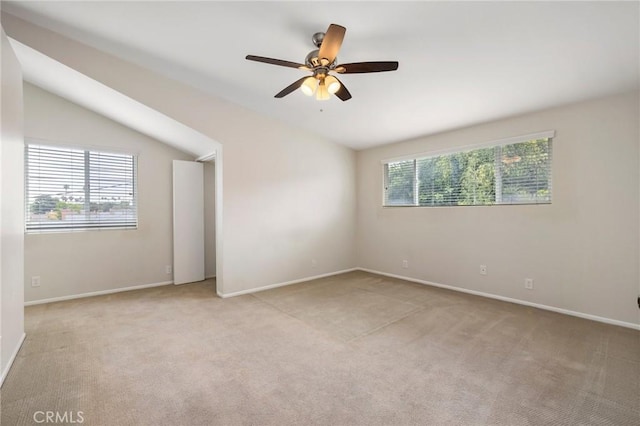 empty room featuring a ceiling fan, baseboards, vaulted ceiling, and light carpet
