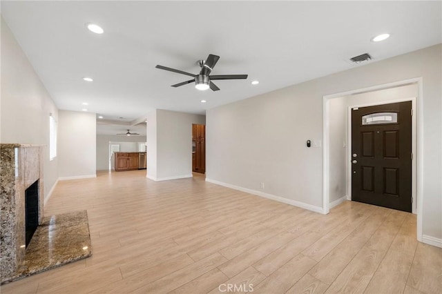 unfurnished living room with a fireplace, ceiling fan, visible vents, and light wood-type flooring