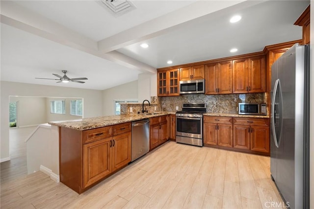 kitchen featuring backsplash, brown cabinets, a peninsula, light wood finished floors, and stainless steel appliances