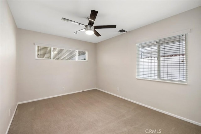 carpeted empty room with baseboards, a ceiling fan, and visible vents