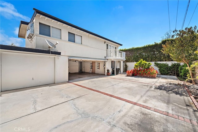 rear view of house featuring an attached garage, stucco siding, a balcony, and concrete driveway