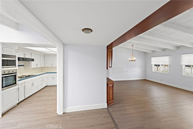 kitchen featuring light countertops, cooktop, baseboards, an inviting chandelier, and stainless steel oven