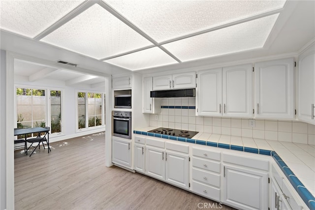 kitchen featuring light wood-style floors, tile counters, white cabinets, tasteful backsplash, and appliances with stainless steel finishes