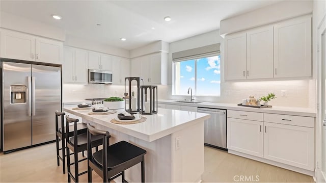 kitchen featuring white cabinets, appliances with stainless steel finishes, a sink, light countertops, and backsplash