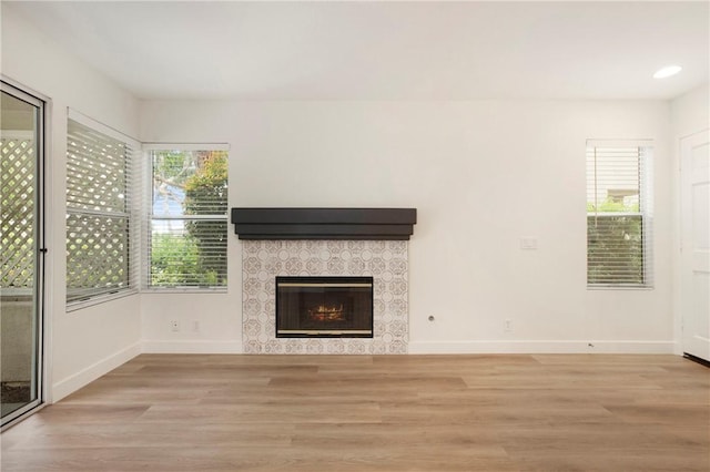unfurnished living room with recessed lighting, baseboards, a tiled fireplace, and wood finished floors