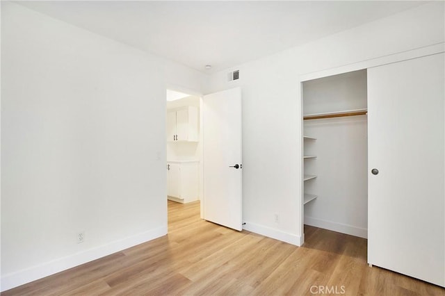 unfurnished bedroom with light wood-type flooring, baseboards, visible vents, and a closet