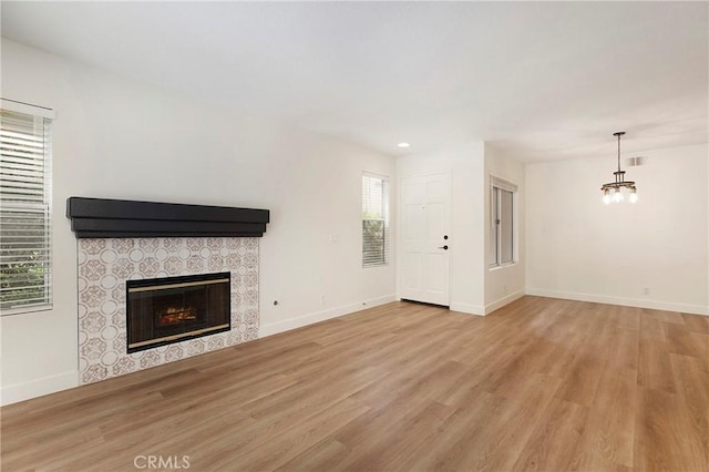 unfurnished living room featuring a tile fireplace, wood finished floors, baseboards, a notable chandelier, and recessed lighting