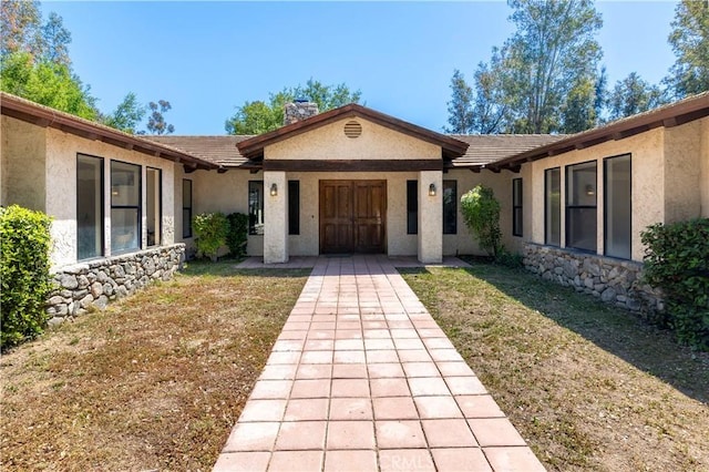 doorway to property with stucco siding, a yard, and a chimney