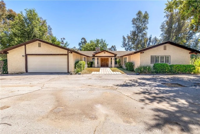 ranch-style home featuring a garage, stucco siding, a chimney, and driveway