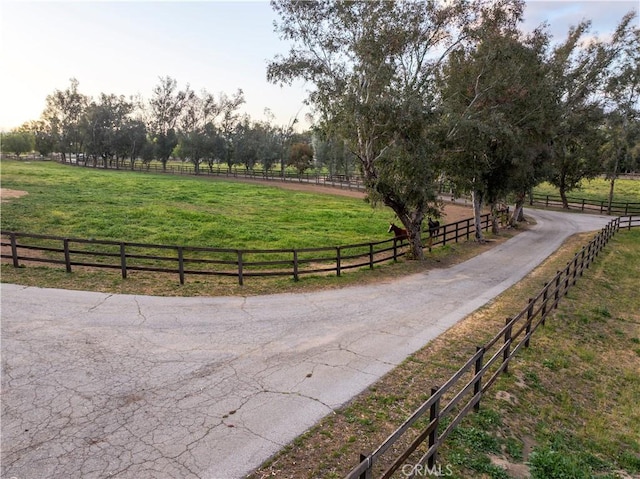 view of property's community with a lawn, a rural view, and fence