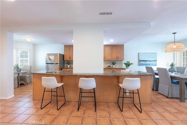 kitchen with backsplash, freestanding refrigerator, a breakfast bar, and visible vents