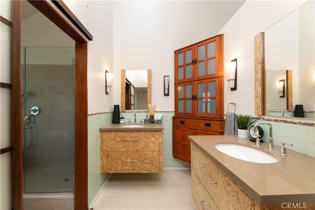 full bath featuring a sink, tile walls, a stall shower, and two vanities