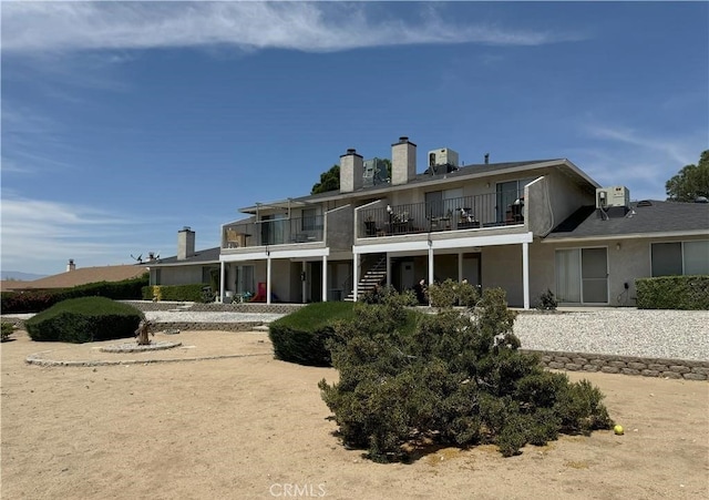 rear view of property with stucco siding, a chimney, a balcony, and stairs