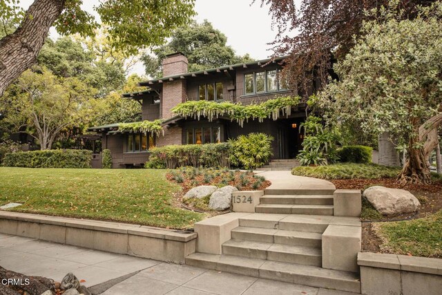 view of front facade featuring a chimney, stairs, and a front lawn