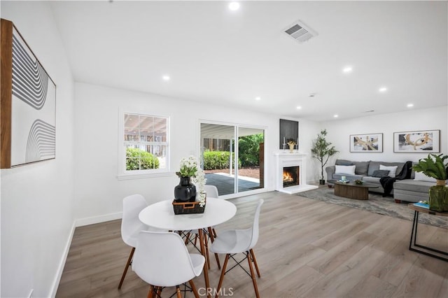 dining space with a warm lit fireplace, light wood-style flooring, recessed lighting, baseboards, and visible vents