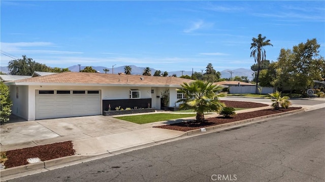 single story home featuring a garage, a mountain view, a front lawn, concrete driveway, and stucco siding