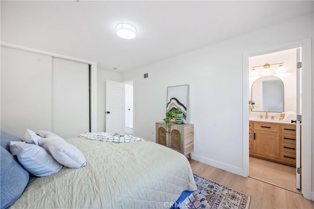 bedroom featuring visible vents, a closet, light wood-type flooring, a sink, and ensuite bath