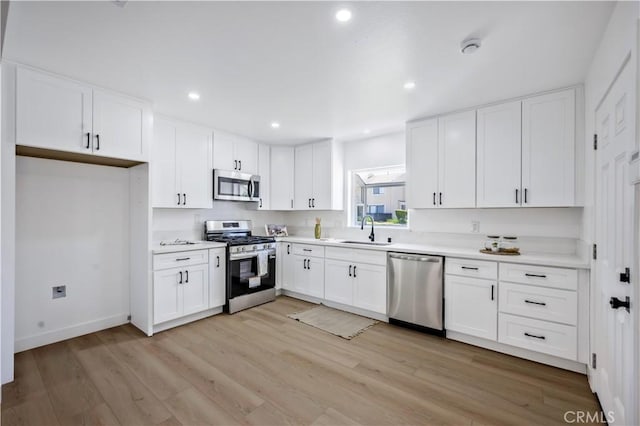 kitchen with stainless steel appliances, white cabinetry, a sink, and light wood-style flooring