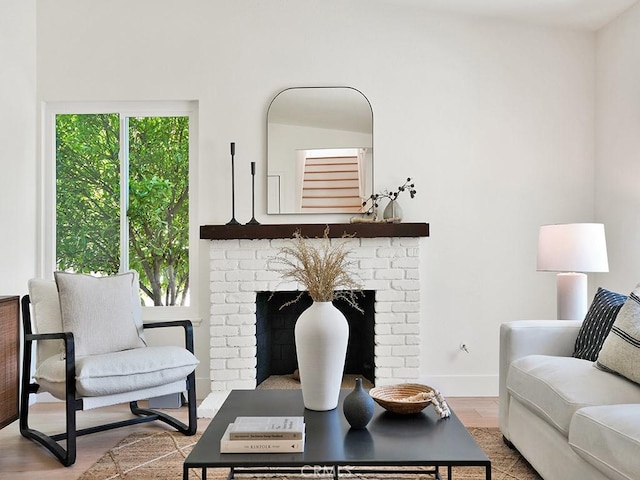 living room with baseboards, a brick fireplace, and wood finished floors