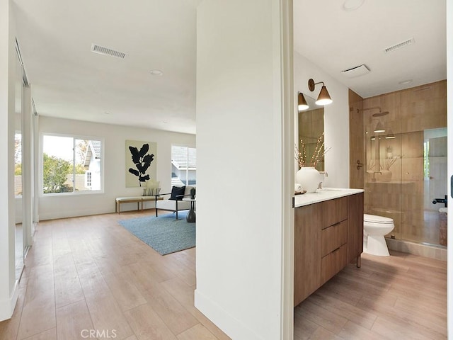 hallway featuring visible vents, a sink, baseboards, and light wood-type flooring