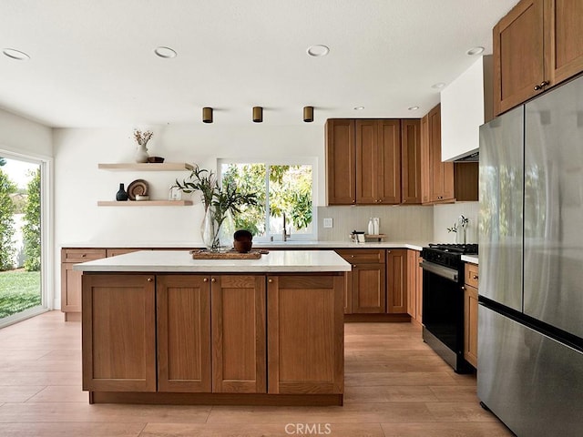 kitchen featuring gas range, a center island, open shelves, light countertops, and freestanding refrigerator