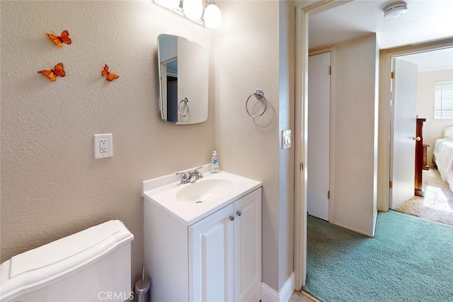 bathroom featuring toilet, a textured wall, and vanity