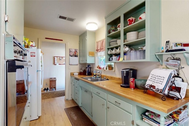 kitchen featuring visible vents, freestanding refrigerator, stainless steel oven, a sink, and light wood-style flooring
