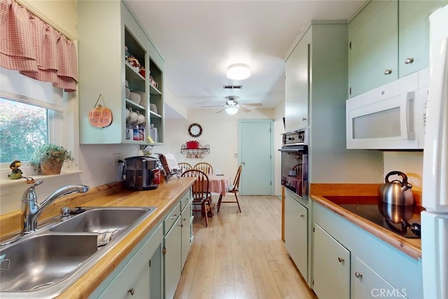 kitchen with a ceiling fan, oven, white microwave, light wood-type flooring, and a sink