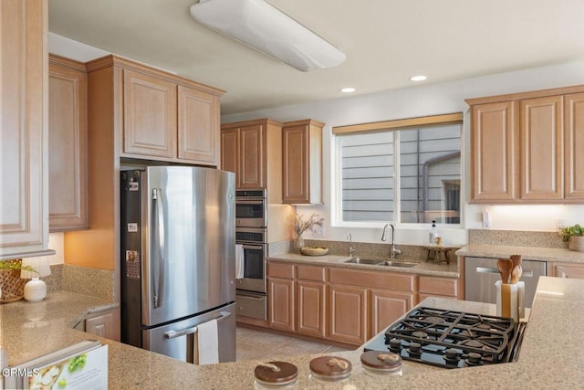 kitchen featuring light brown cabinets, light stone counters, a sink, appliances with stainless steel finishes, and a warming drawer
