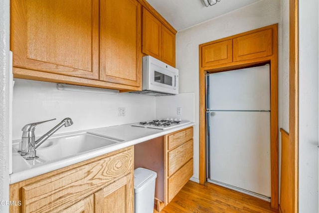 kitchen with light wood-style floors, a sink, white appliances, and light countertops