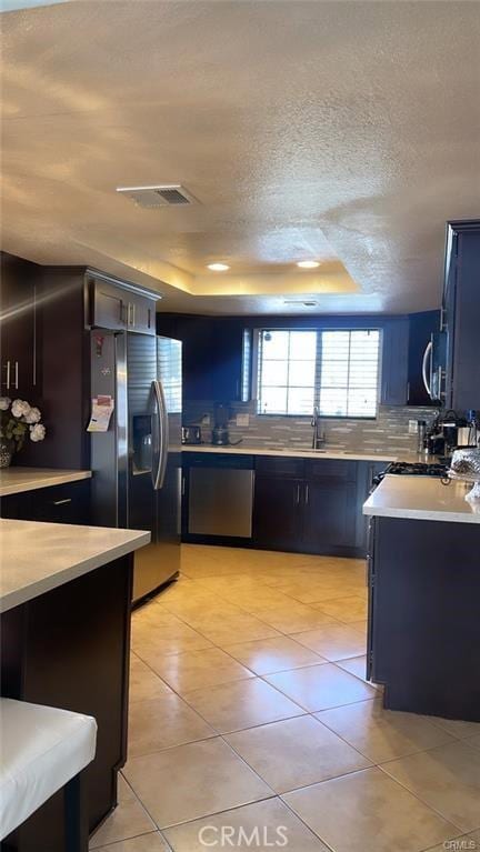 2285 W 2nd Ave, San Bernardino, CA 92407 - kitchen featuring appliances with stainless steel finishes, light countertops, light tile patterned floors, a sink, and decorative backsplash