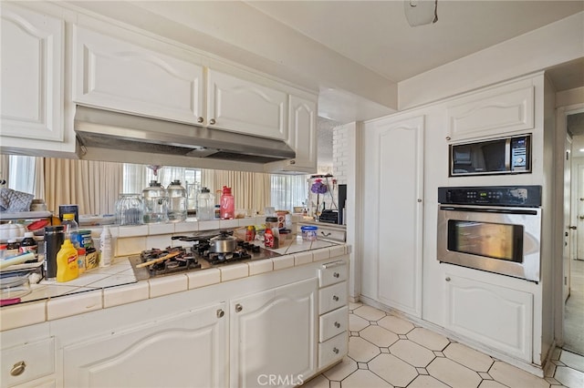 10139 Hayvenhurst Ave, North Hills, CA 91343 - kitchen with oven, tile counters, black microwave, white cabinetry, and under cabinet range hood