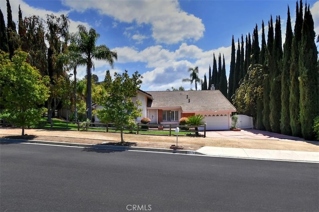 view of property hidden behind natural elements featuring an attached garage, fence, and driveway