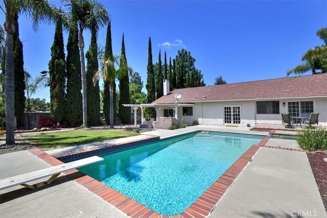 outdoor pool with a patio and a diving board